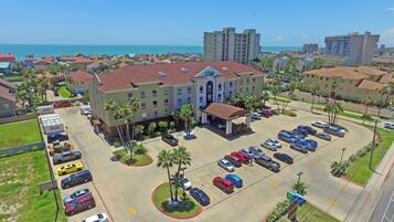 A hotel with a parking lot, a beach view, and a large building in the background.