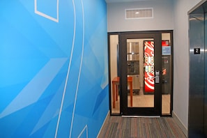 A hotel hallway with a blue geometric wall design, a glass door leading to a room with a red and white sign, and an elevator with the number 2.