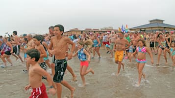 Une plage bondée où l’on voit des gens courir et jouer dans l’eau.