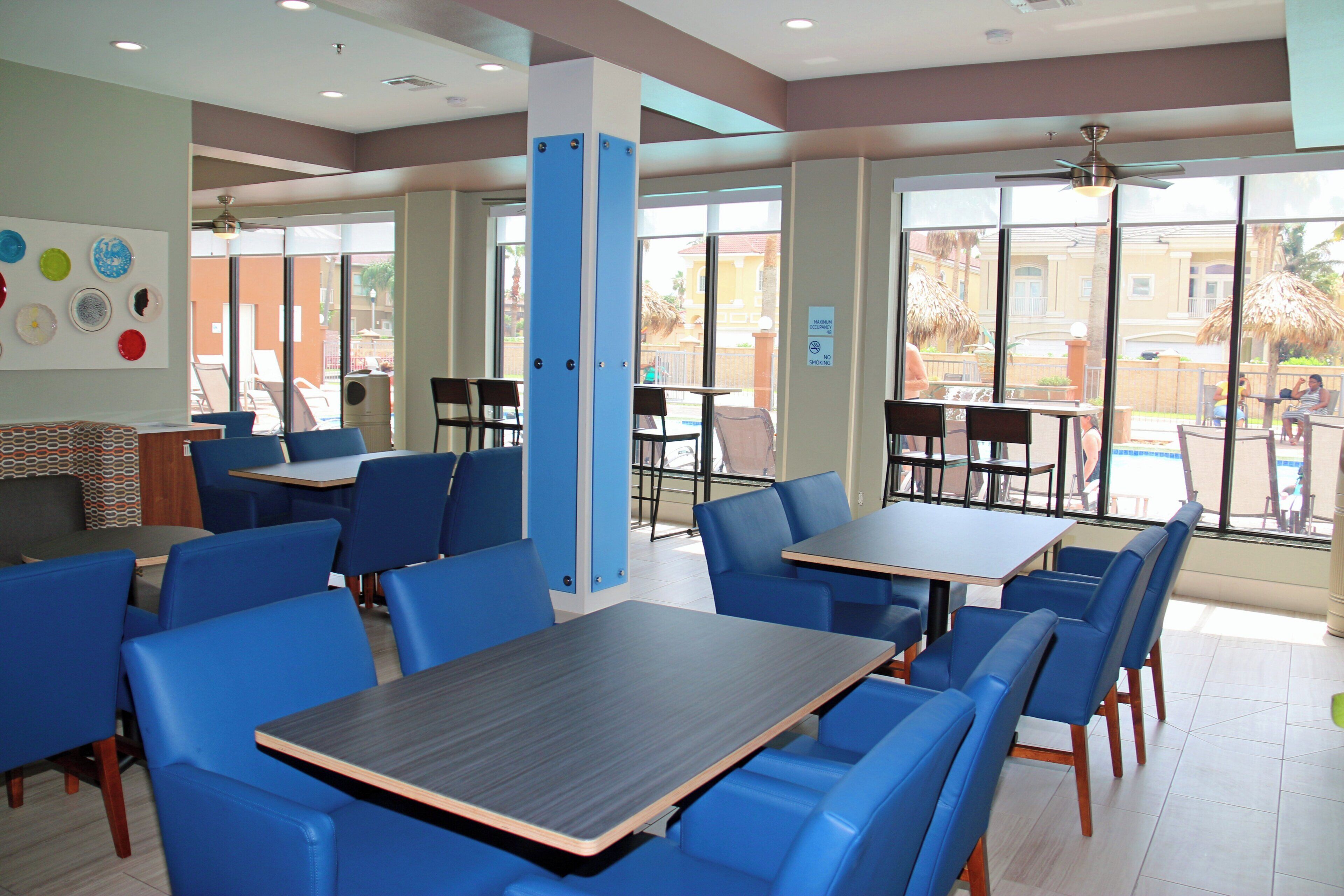 A restaurant with blue chairs and tables, large windows, and a view of the outside.