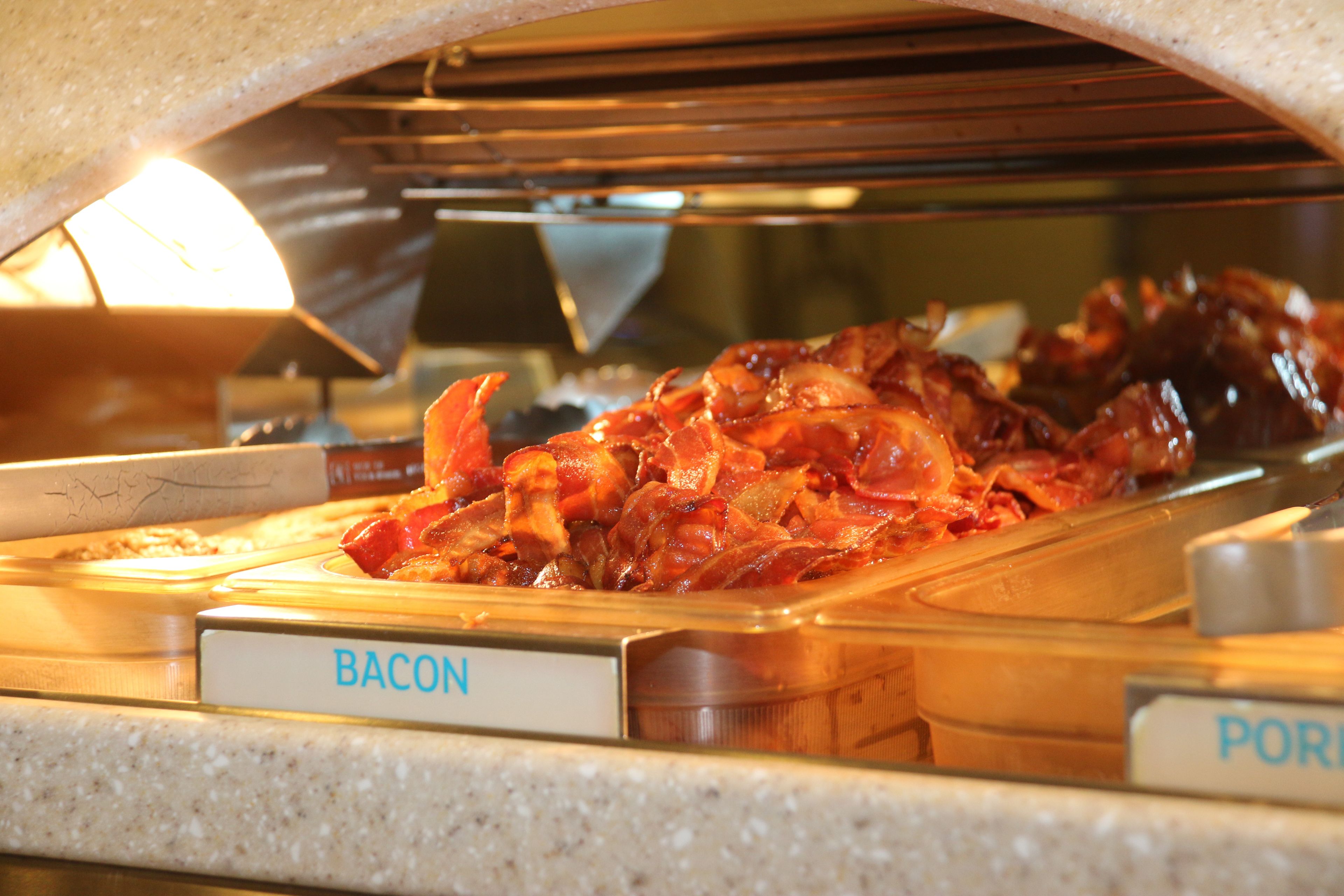 A buffet with labeled sections for bacon and pork.