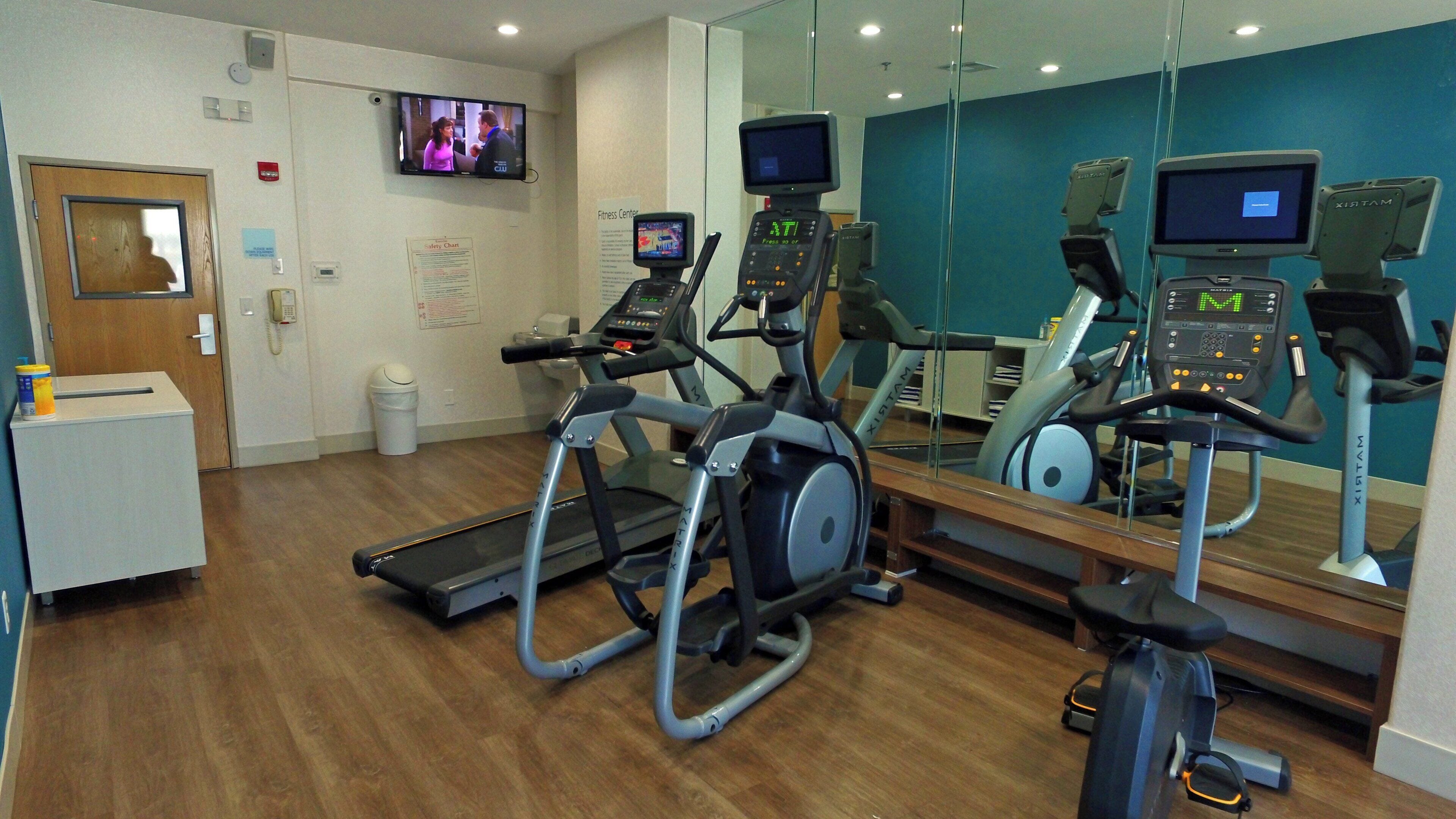 A fitness center with treadmills, a TV screen, and a mirror reflecting the equipment.
