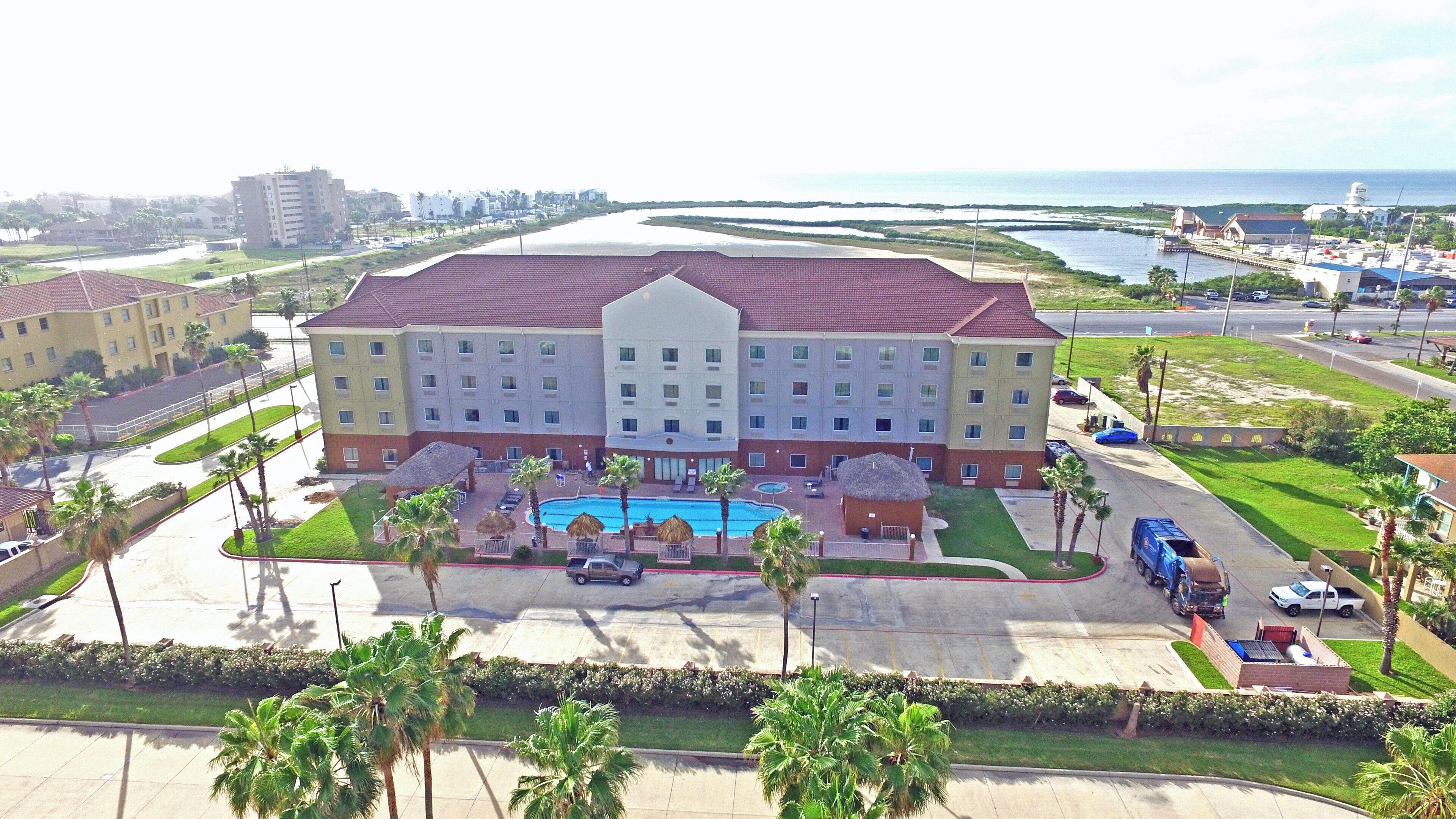 A large hotel with multiple floors, a swimming pool, and a parking lot.