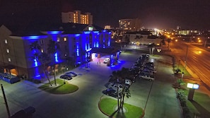 Un hotel con estacionamiento, entrada cubierta y un edificio con luces azules iluminadas.