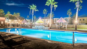 A swimming pool with lounge chairs, palm trees, and umbrellas.