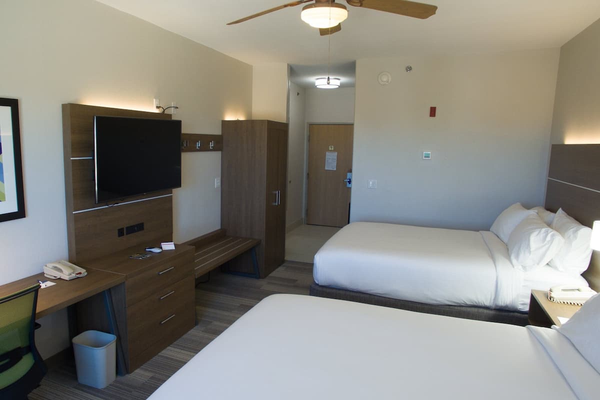 A hotel room with a bed, a desk with a telephone, a television, and a ceiling fan.