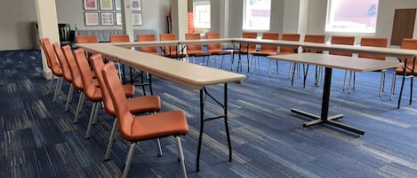 Un salón de conferencias con filas de sillas naranjas y mesas, piso alfombrado y cuadros en las paredes.