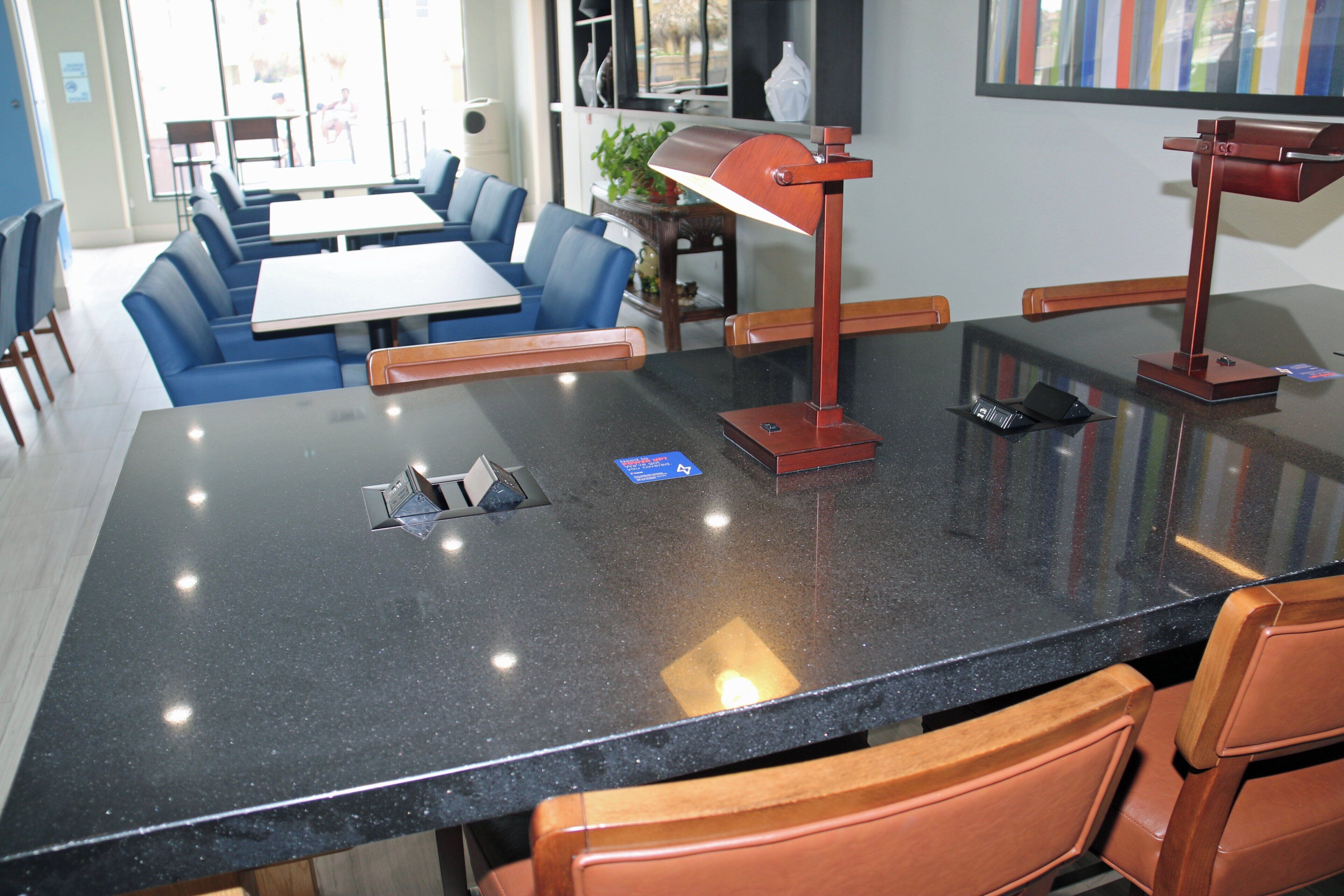 Un espace repas moderne avec une table en granit noir, des chaises recouvertes d’un tissu bleu et une suspension rouge.