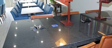 Un espace repas moderne avec une table en granit noir, des chaises recouvertes d’un tissu bleu et une suspension rouge.