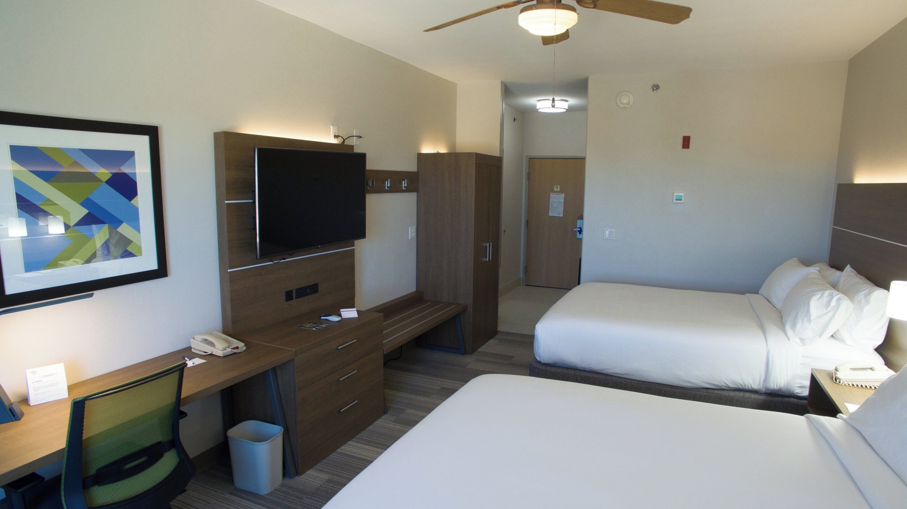 Une chambre d’hôtel équipée d’un lit, d’un bureau avec un téléphone, d’une télévision et d’un ventilateur de plafond.