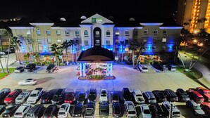 A Holiday Inn Express & Suites with a central atrium, parking lot, and a building facade with illuminated windows.