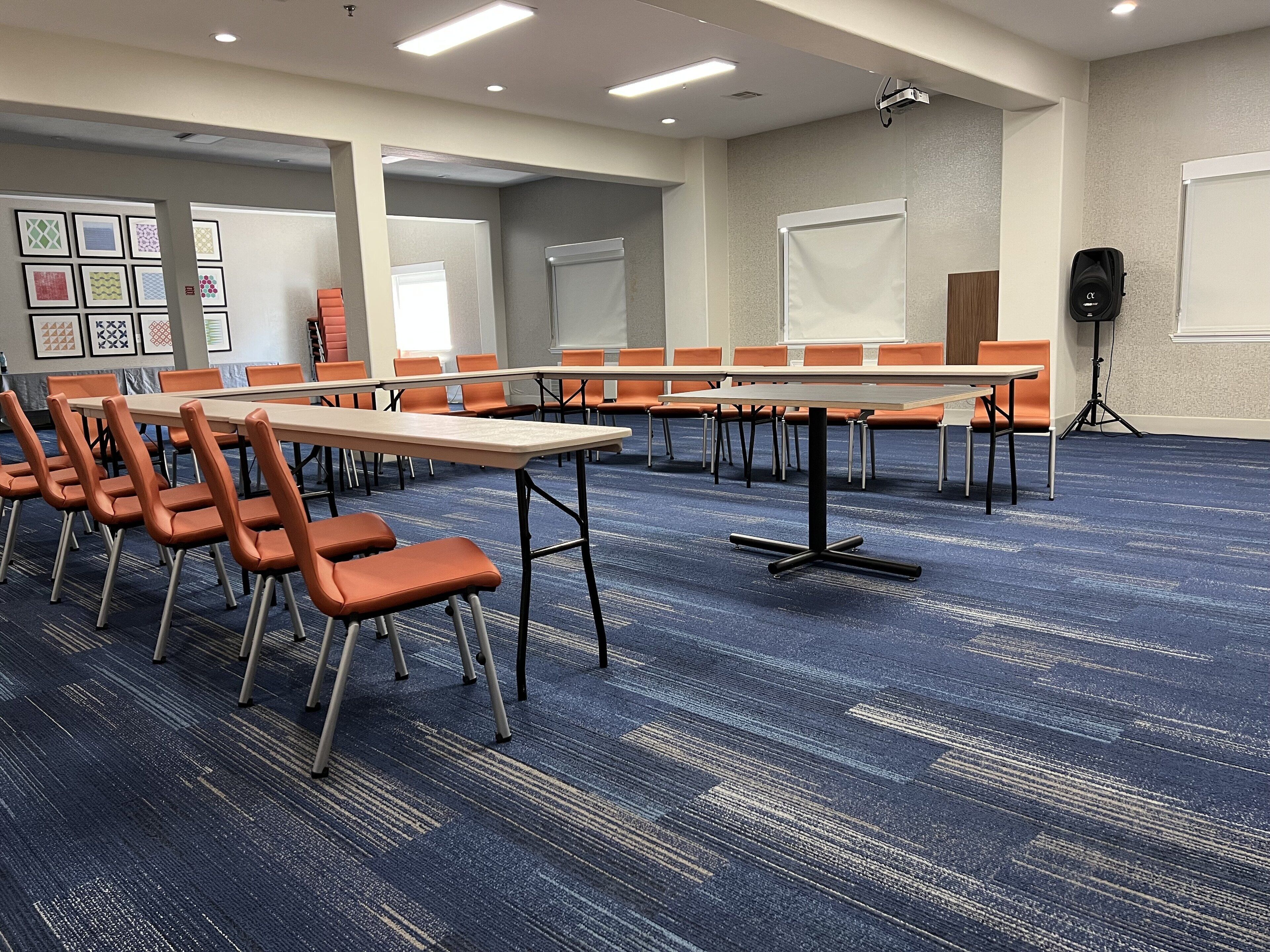 A conference room with tables and chairs, a projector, and a carpeted floor.