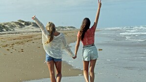 Dos personas caminando sobre una playa arenosa, con el océano al fondo.