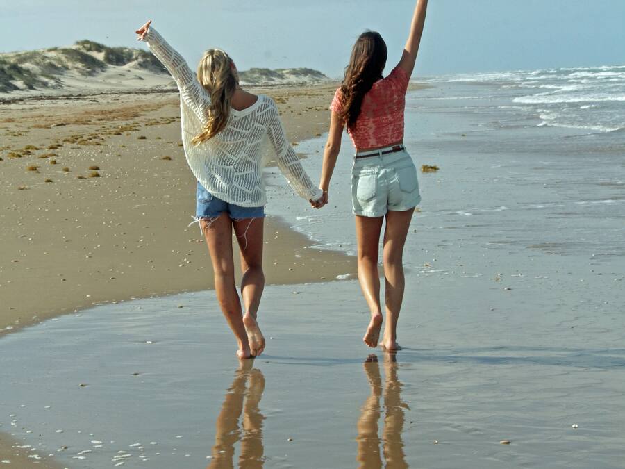 Zwei Personen laufen am Sandstrand, im Hintergrund das Meer.