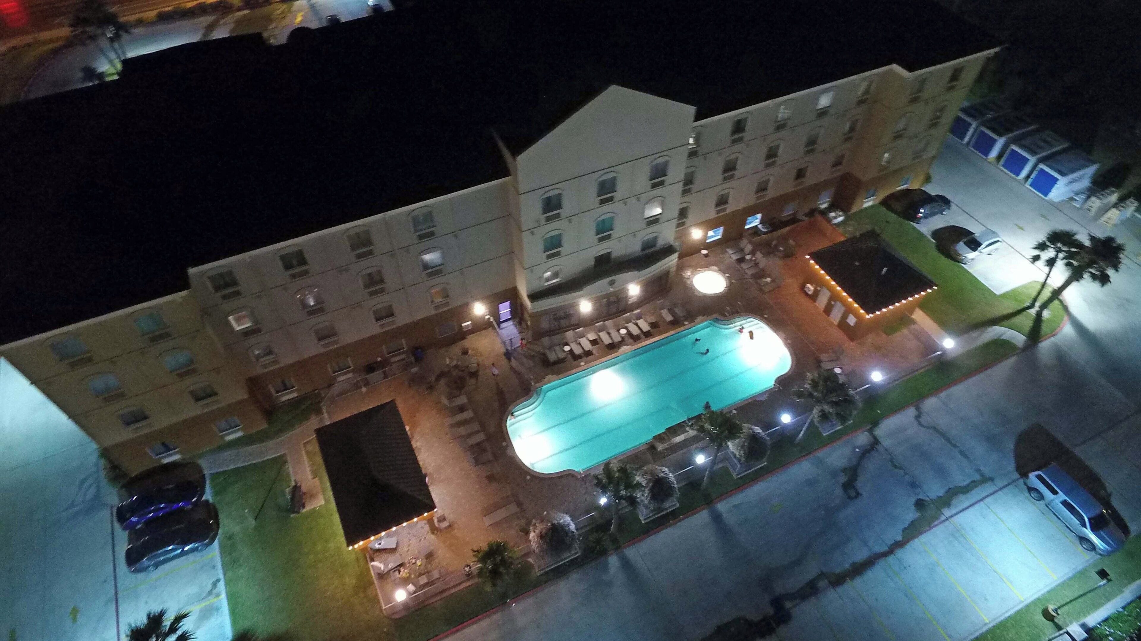 A hotel with a swimming pool, multiple balconies, and a parking area.