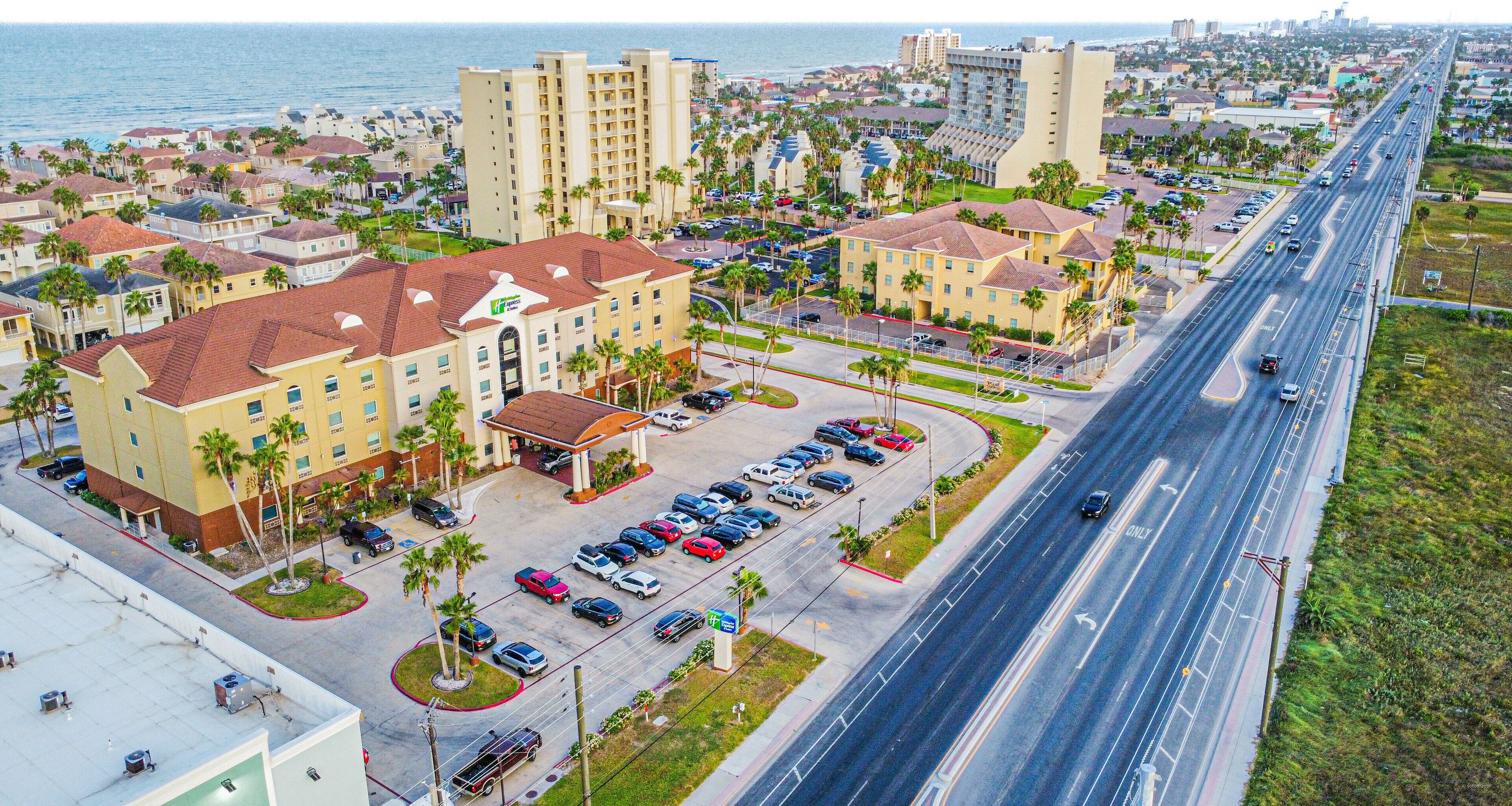 A hotel with multiple buildings, a parking lot, and a road with vehicles.