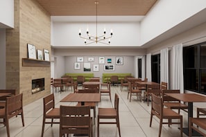 A modern dining area with wooden tables and chairs, a central seating area with a green sofa, and a fireplace.