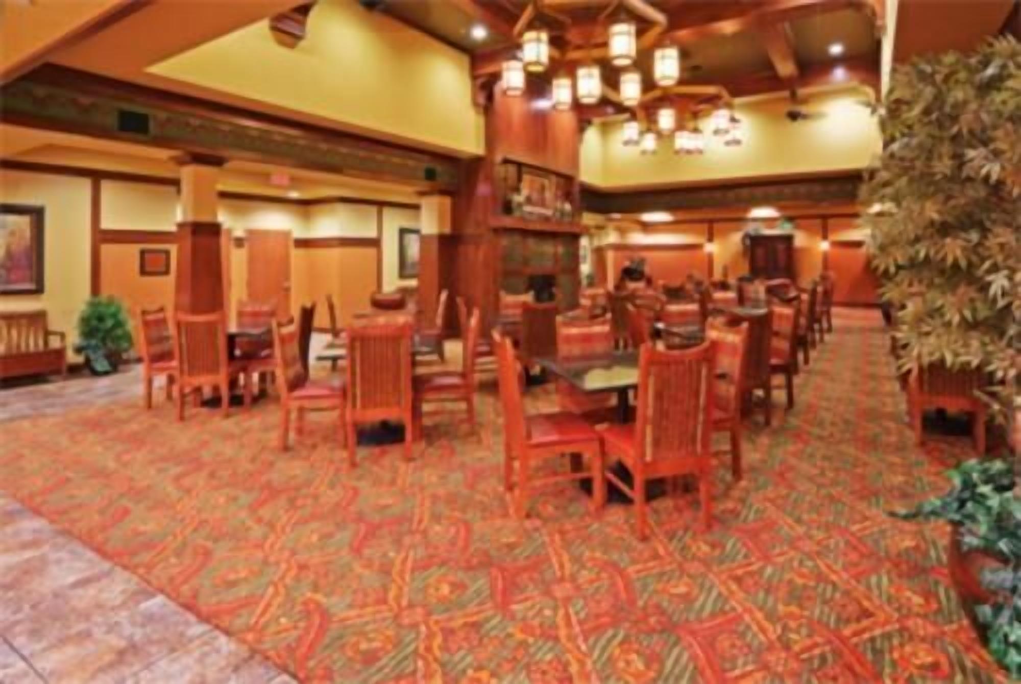 A spacious dining area with multiple tables and chairs, a patterned carpet, and a warm color scheme.