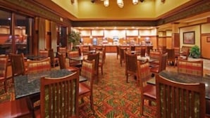 A hotel lobby with wooden chairs and tables, a patterned carpet, and a reception desk in the background. - Country Inn & Suites by Radisson, Springfield Downtown (Springfield)