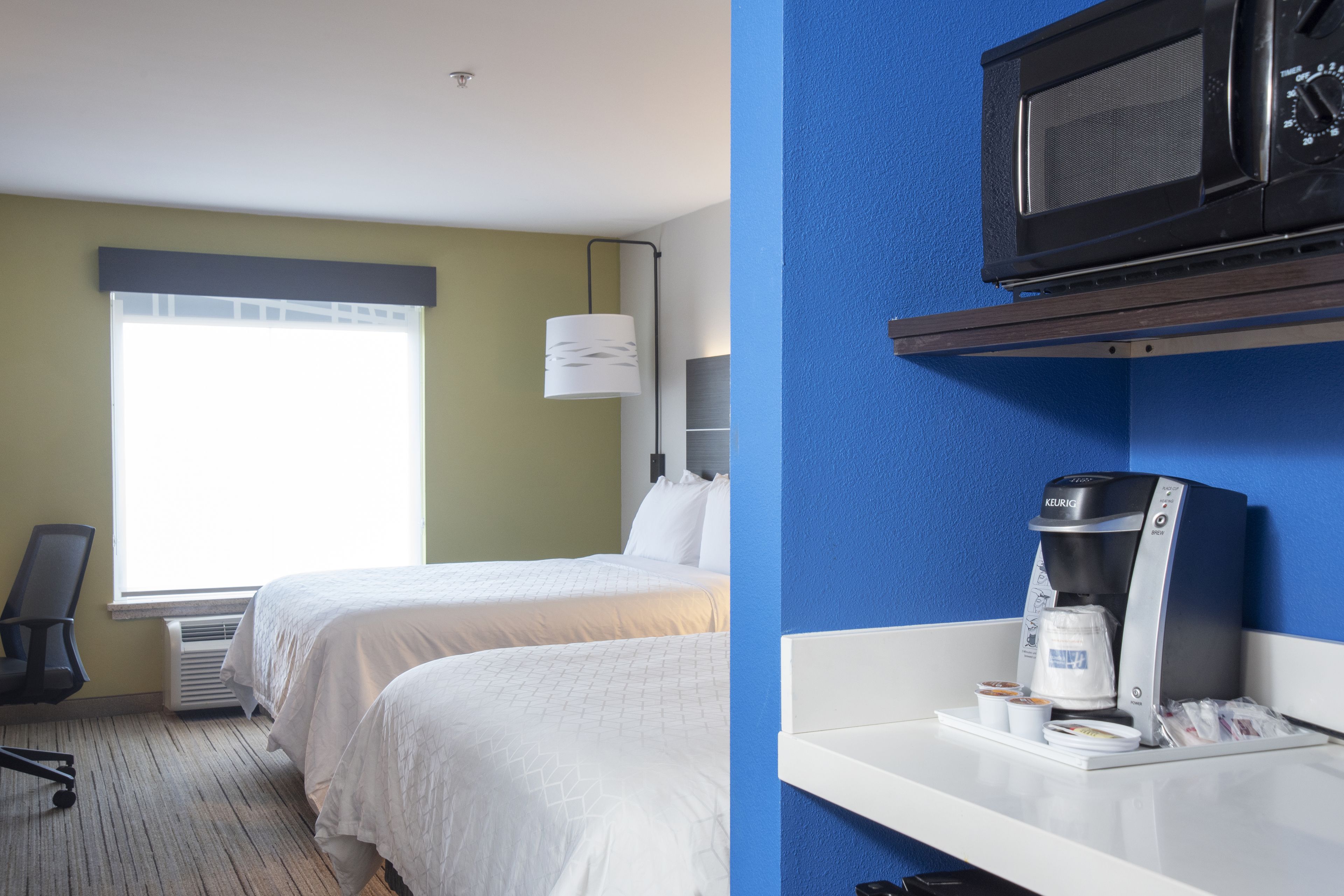 A hotel room with two beds, a desk with a coffee maker, and a microwave on the wall.