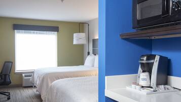 A hotel room with two beds, a desk with a coffee maker, and a microwave on the wall.