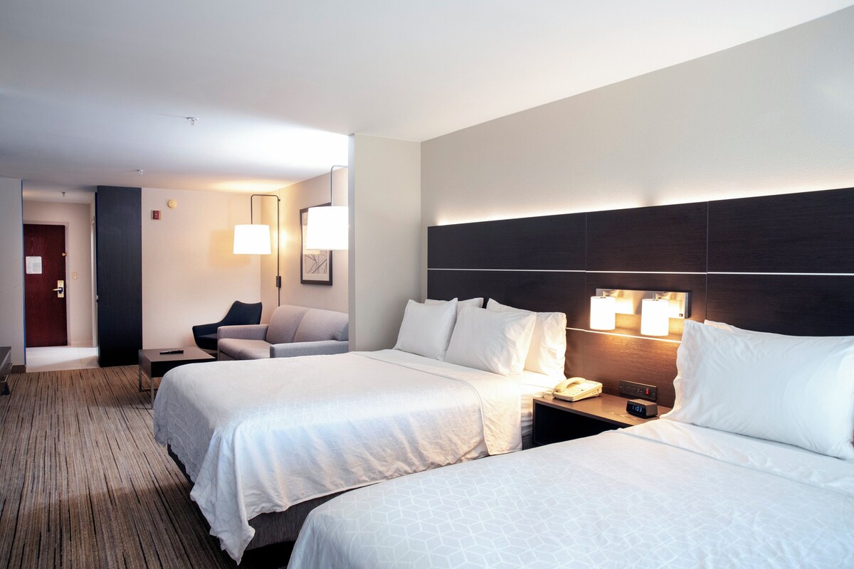 Une chambre d’hôtel avec deux lits, un bureau, une chaise et une lampe.