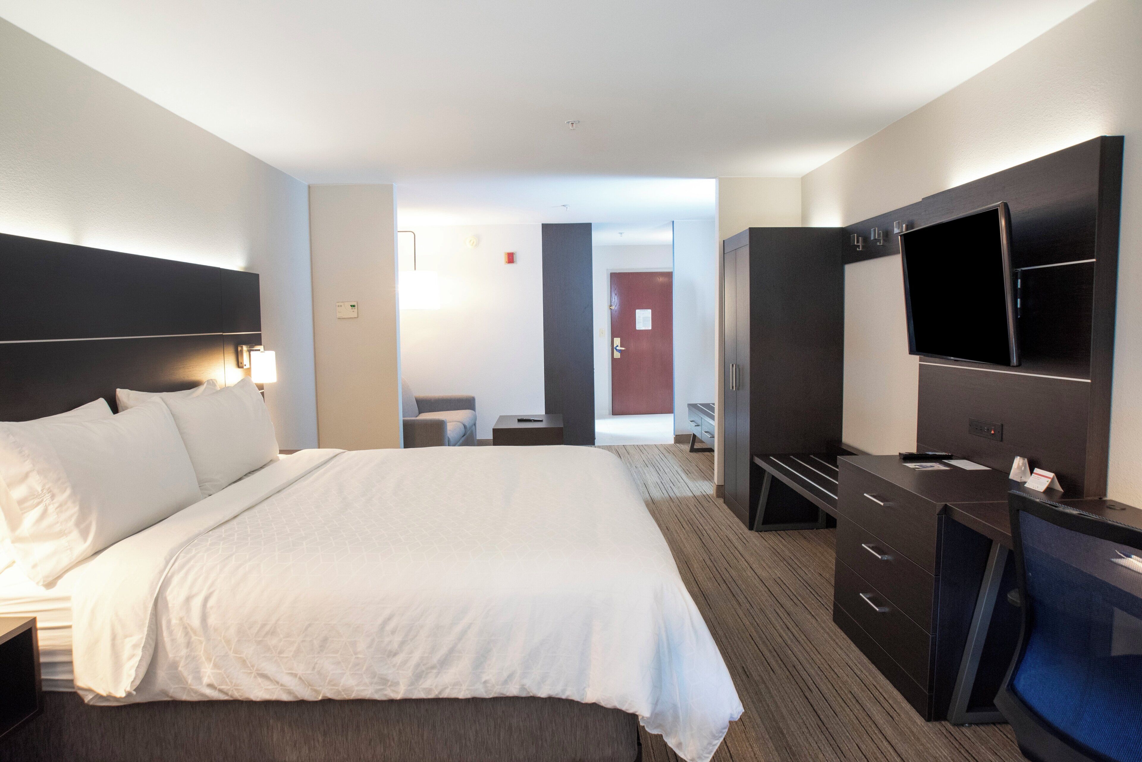 Een hotelkamer met een groot bed, een bureau met een flatscreen televisie, een kledingkast en een deur naar een andere kamer.
