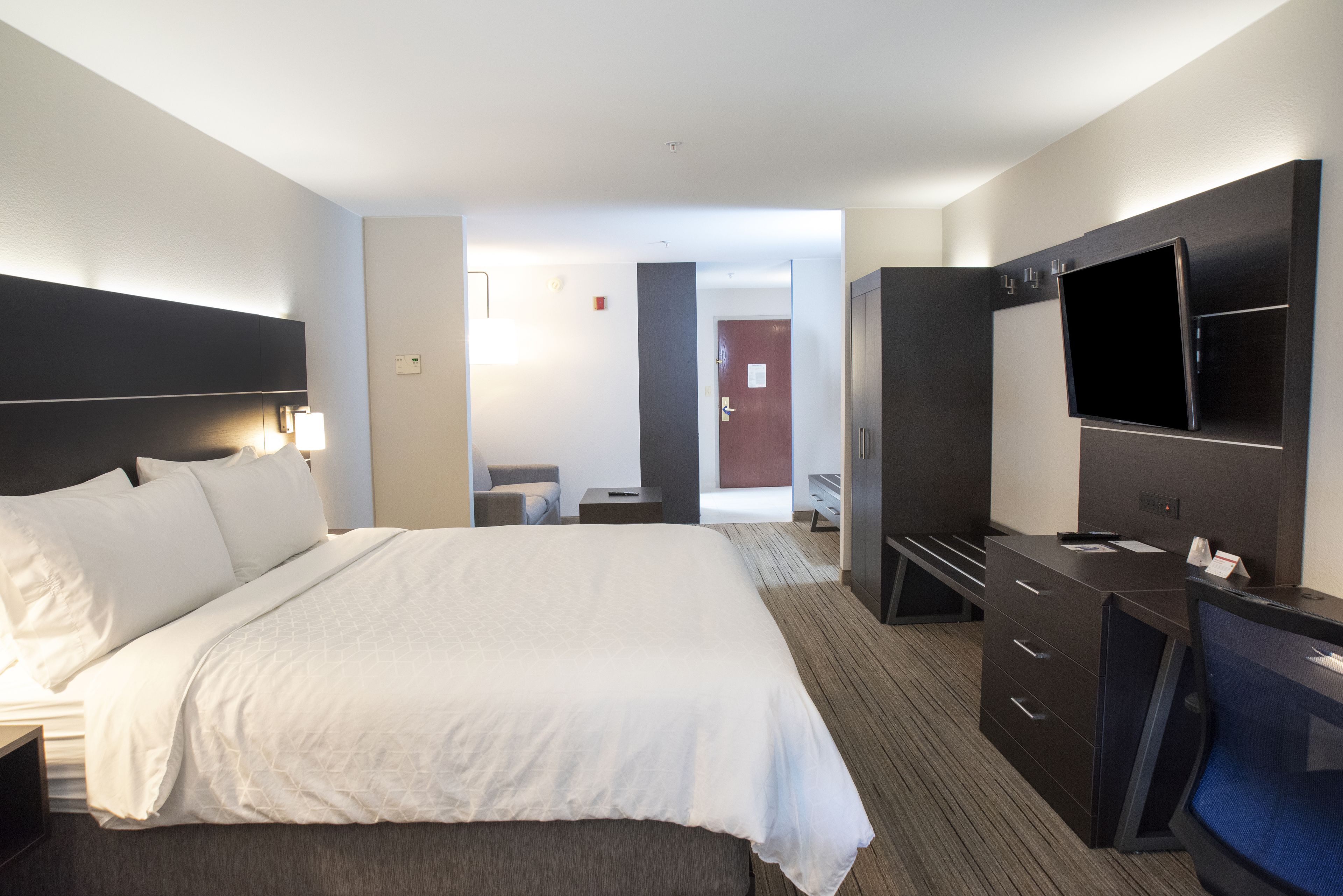 A hotel room with a large bed, a desk with a flat-screen TV, a wardrobe, and a mirror.