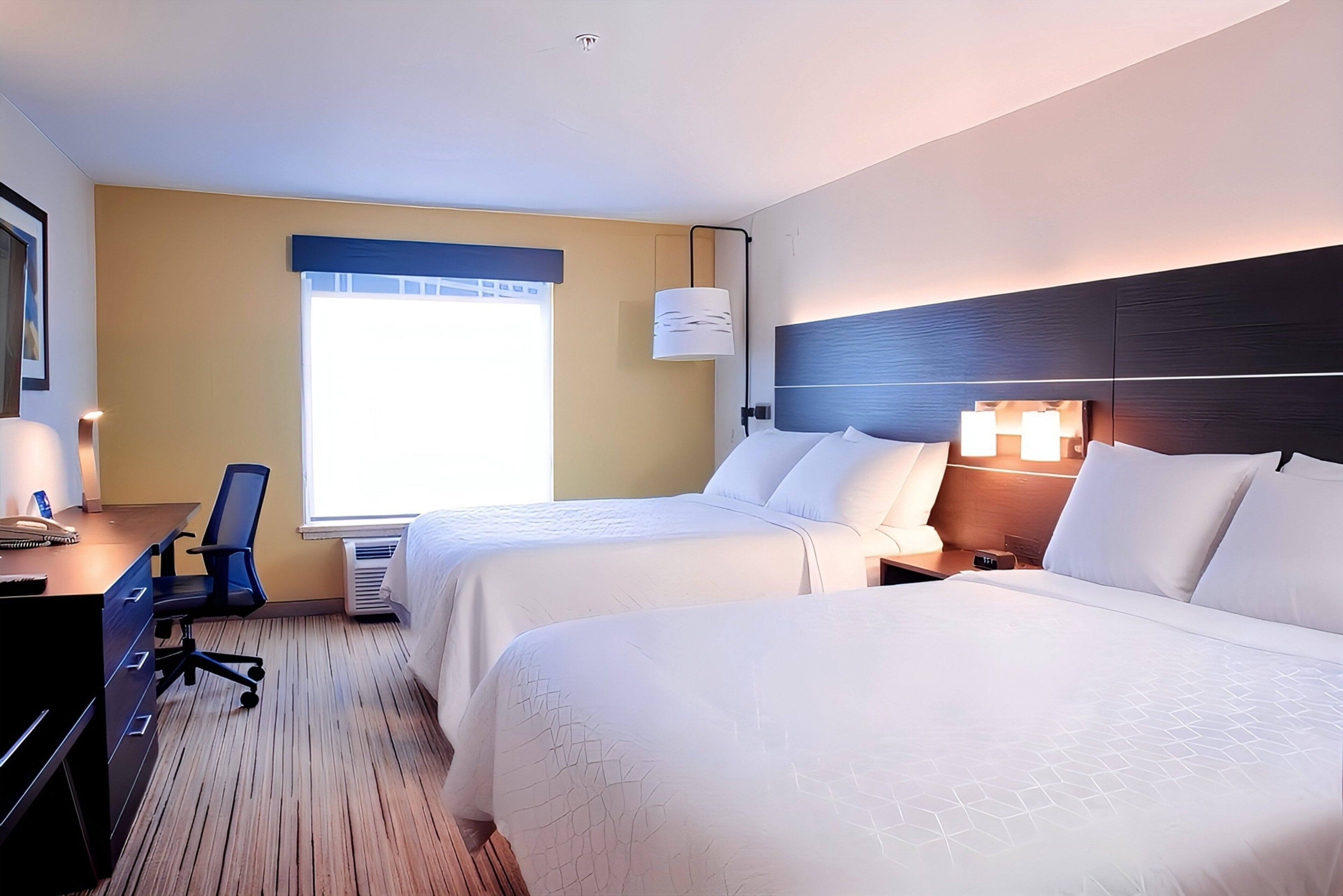 A hotel room with two beds, a desk with a chair, and a window with blinds.