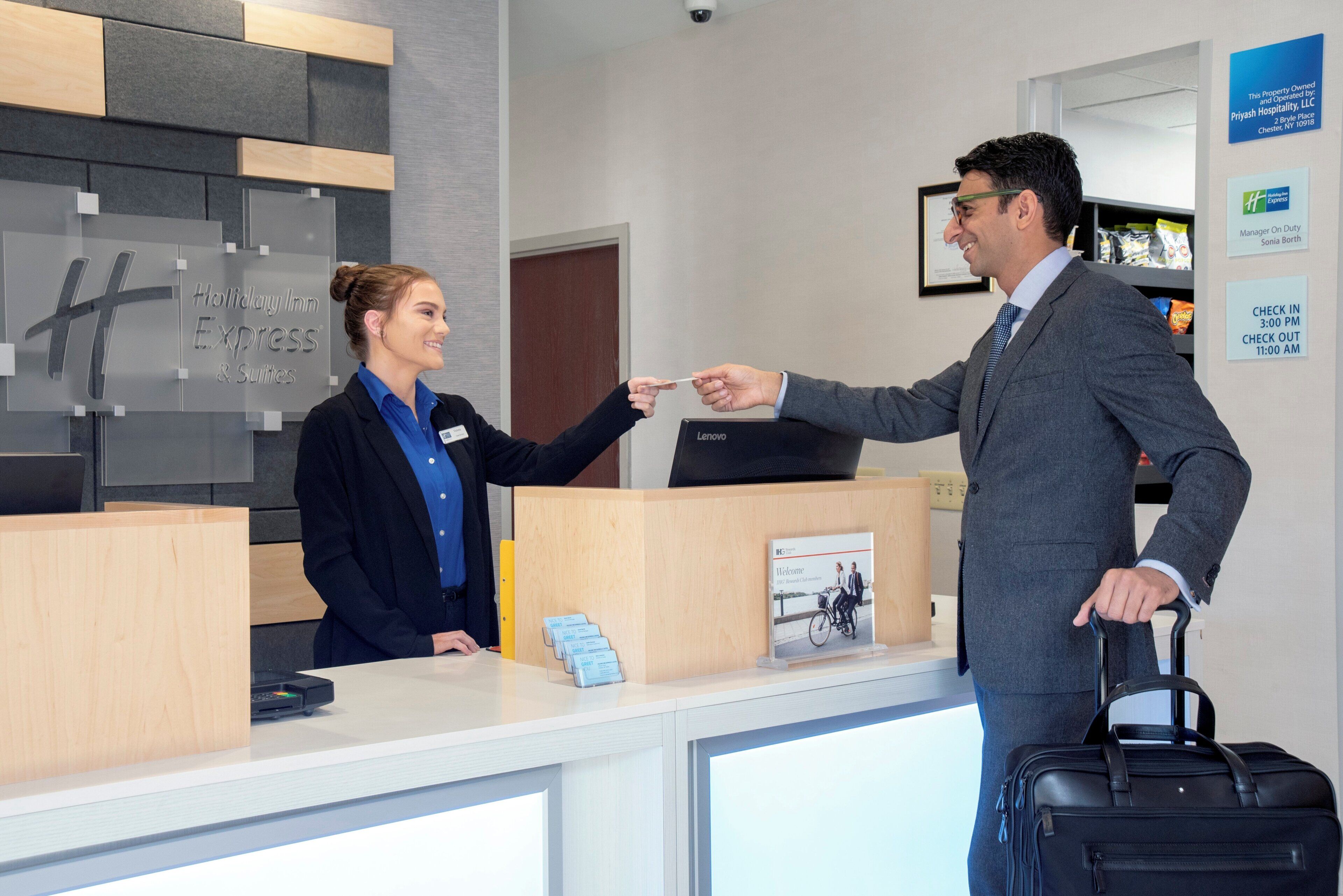 A hotel reception desk with a digital check-in kiosk, a framed welcome sign, and a guest with a suitcase.