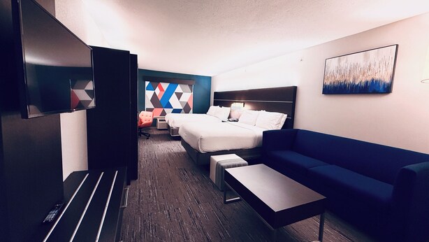 A hotel room with a bed, a sofa, a TV, a desk, and a wall with a geometric pattern. - Holiday Inn Express Hotel & Suites Chester by IHG (Chester)