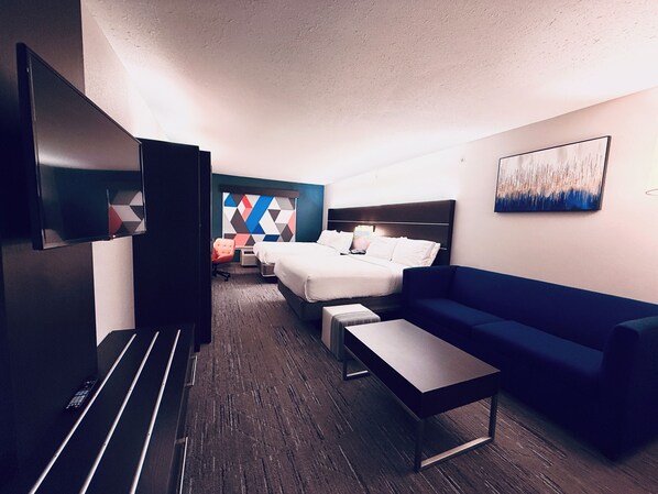 Une chambre d’hôtel comprenant un lit, un canapé, une télévision, un bureau et un mur orné d’un motif géométrique.
