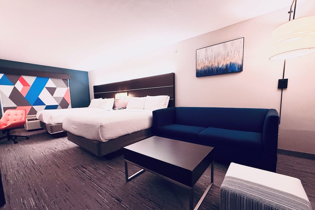 A hotel room with a bed, a sofa, a coffee table, a chair, and a geometric-patterned wall.