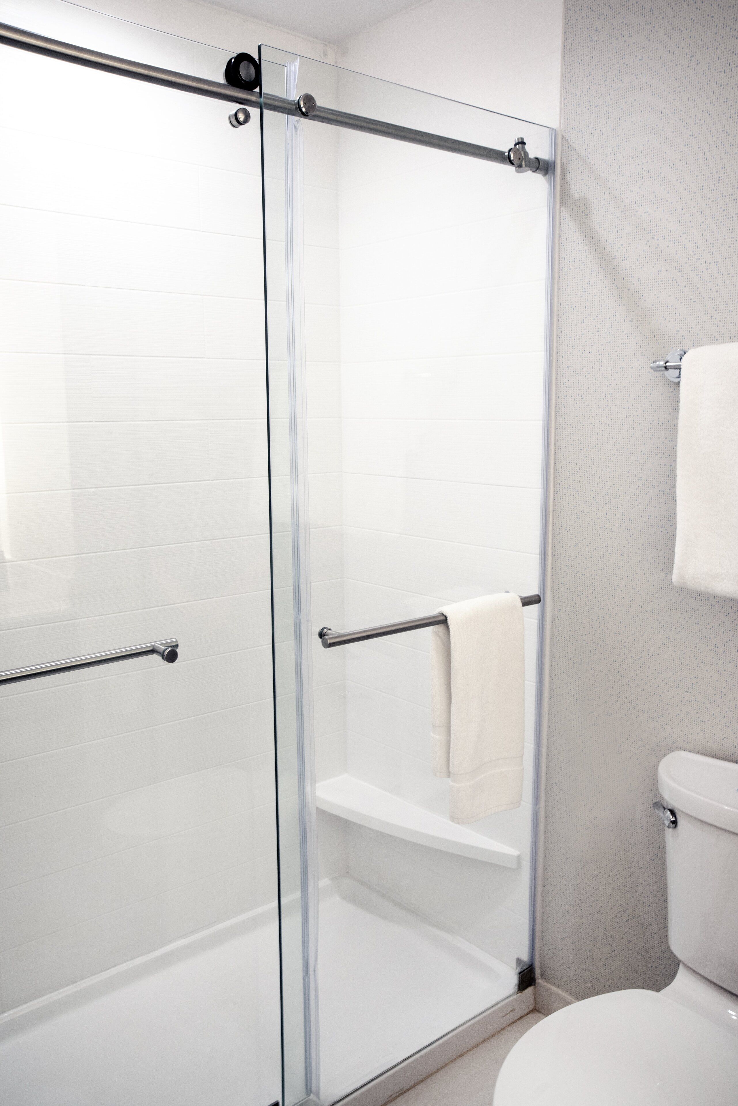 Une salle de bain moderne avec une douche à parois de verre, des toilettes blanches et un porte-serviettes.