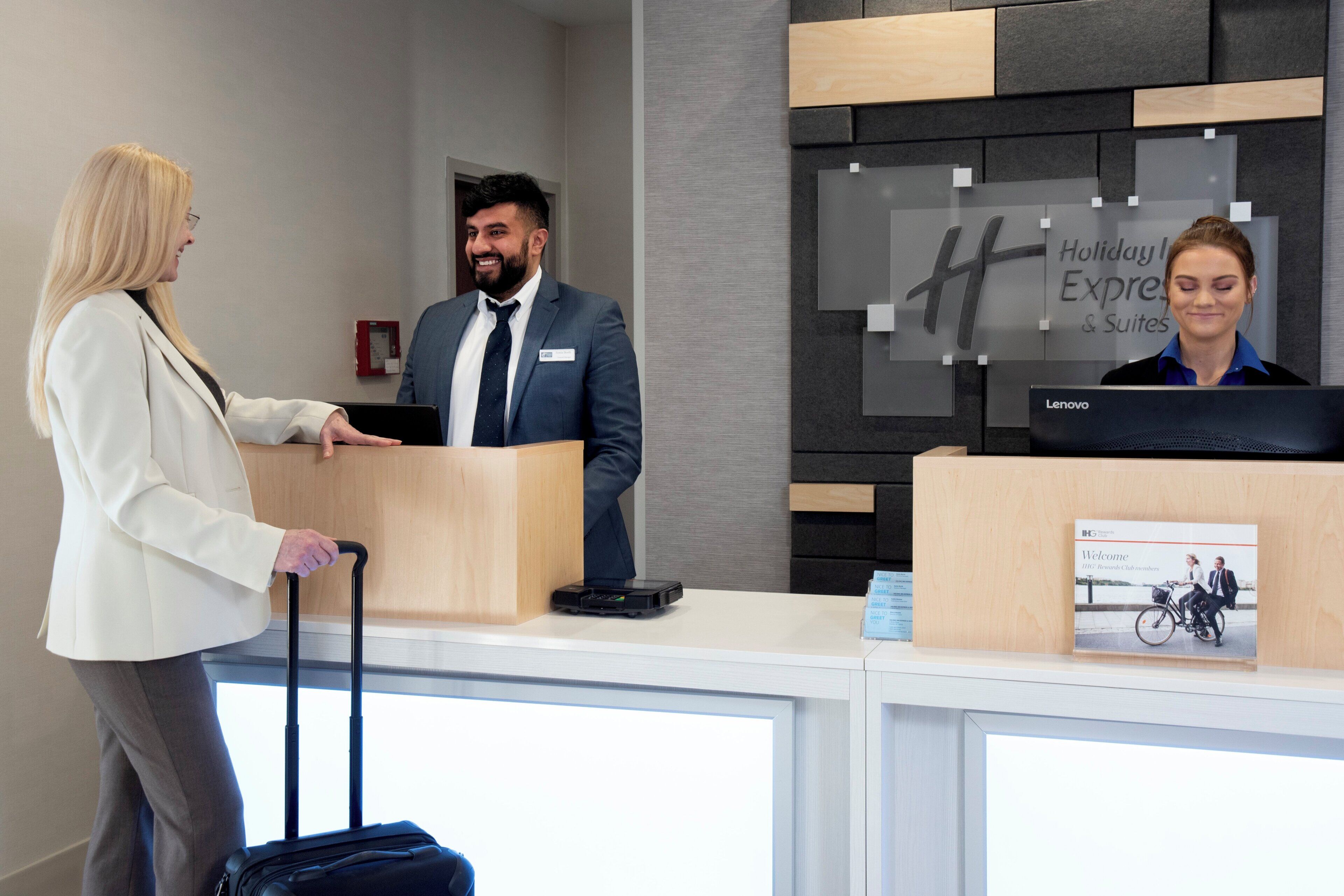 Un mostrador de recepción de hotel con una pantalla digital que muestra el nombre y los servicios del hotel. Hay una placa con el nombre en el mostrador y se ve un ordenador portátil.