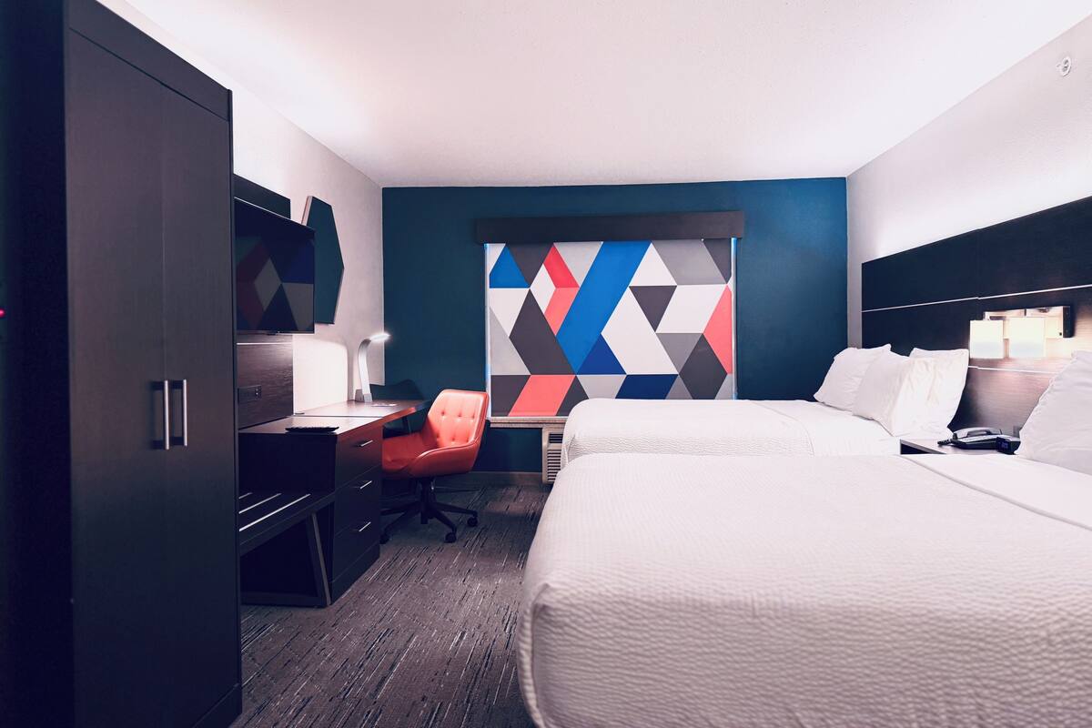 A hotel room with a bed, a desk, a chair, and a colorful geometric wall design.
