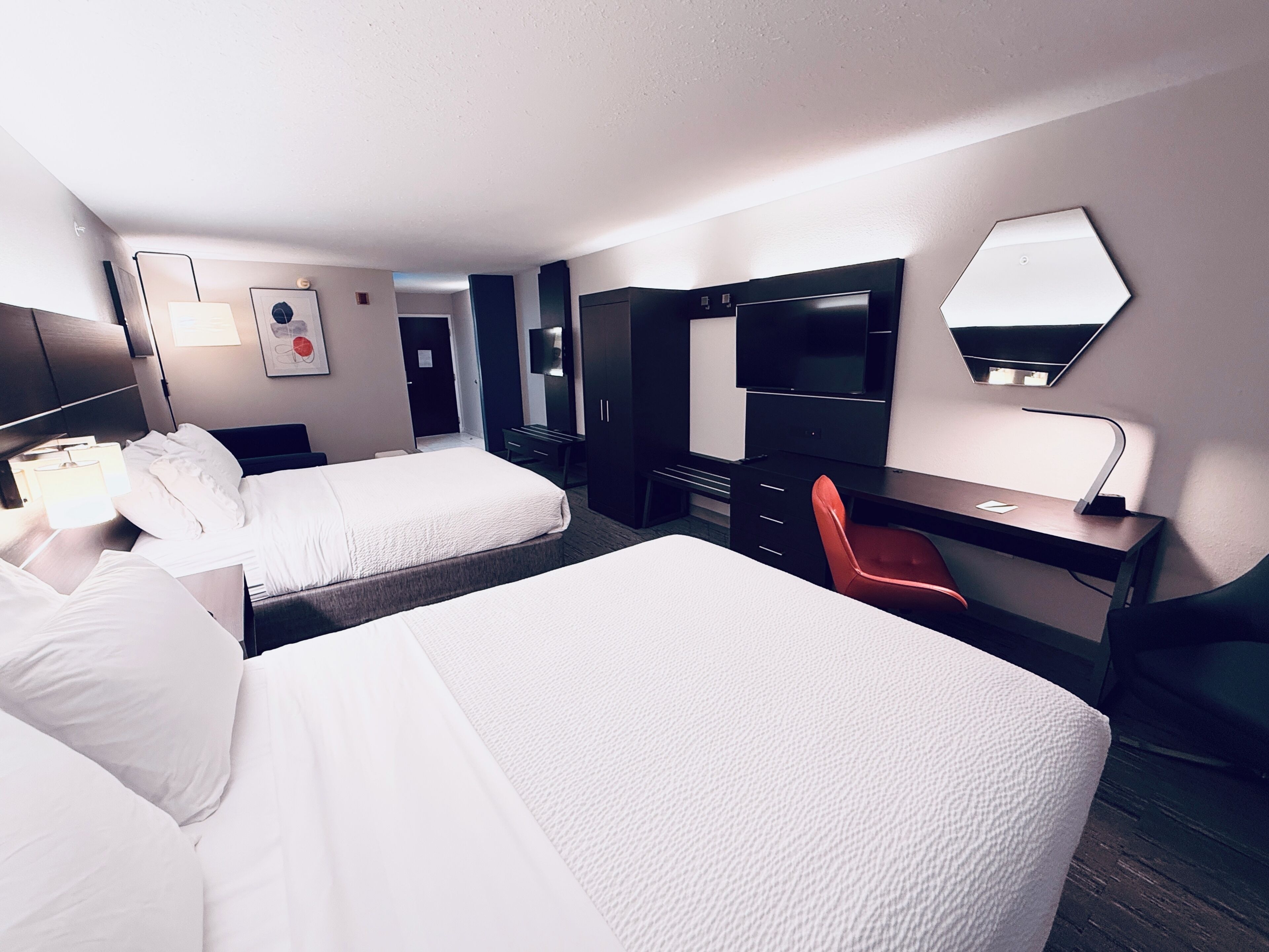 A hotel room with two beds, a desk, a chair, a TV, and a mirror.