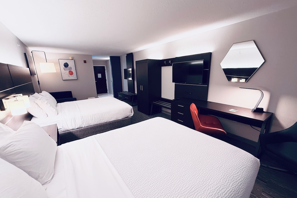 Hotellihuone, jossa on kaksi sänkyä, työpöytä, tuoli, televisio ja peili.