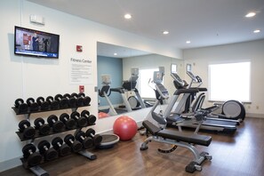 Une salle de sport équipée de tapis de course, de vélos elliptiques, d’un ballon d’exercice rouge et d’un porte-haltères.