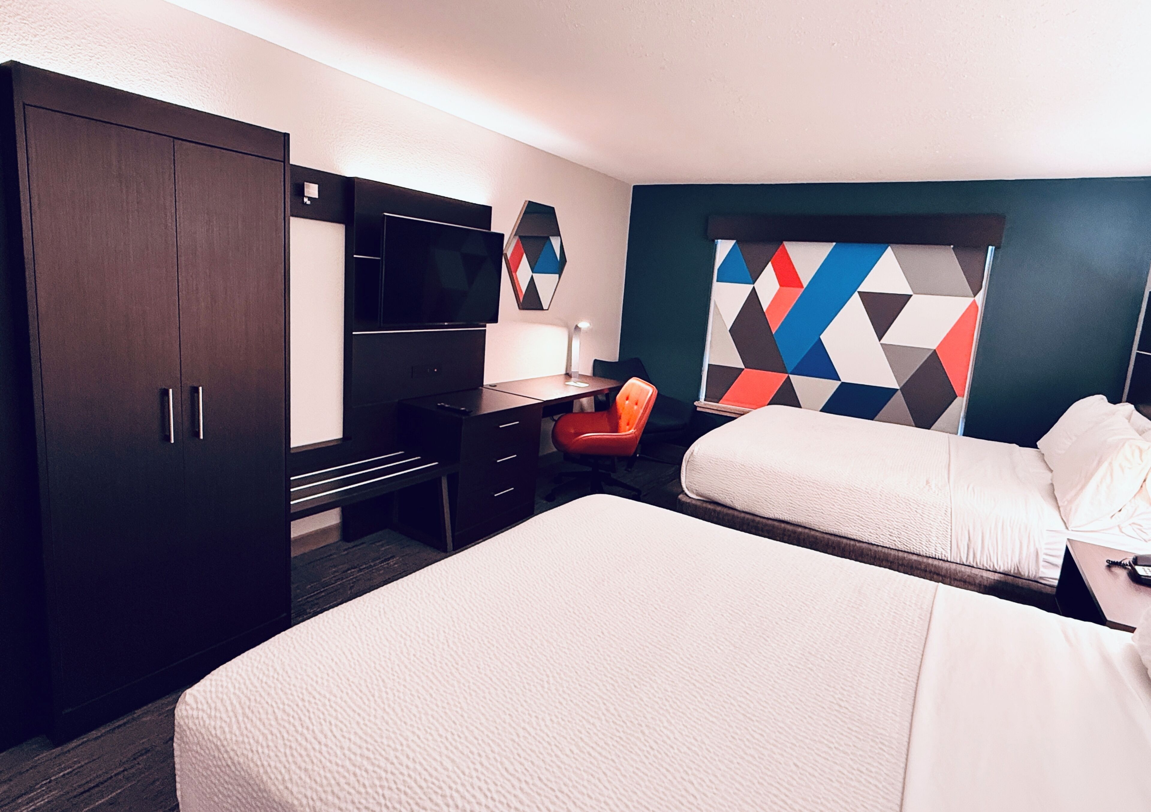 A hotel room with a bed, desk, chair, TV, and a geometric-patterned wall.