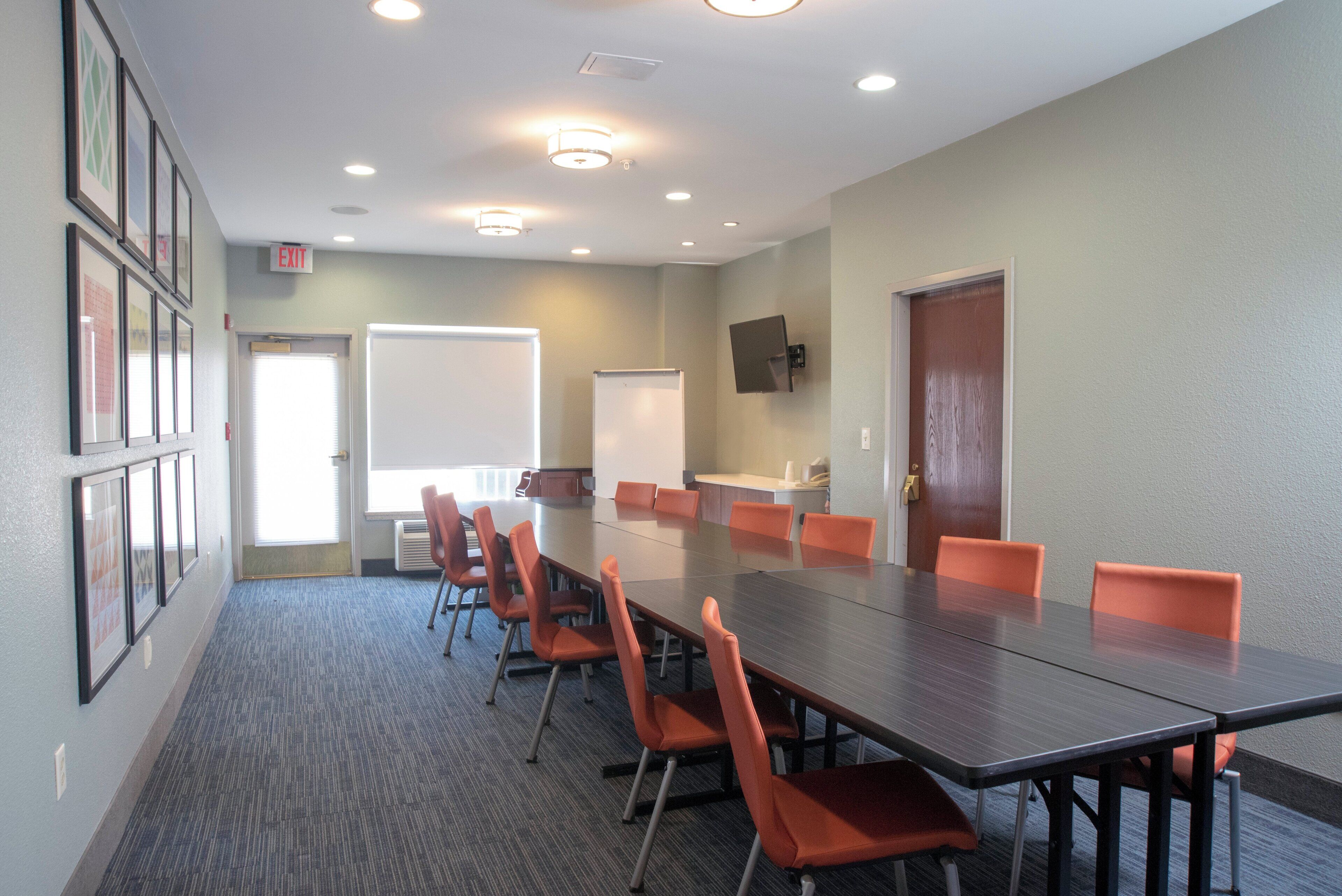 Un salón de conferencias con una larga mesa, sillas color naranja, una pizarra y una puerta.