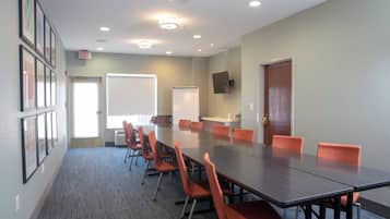 Un salón de conferencias con una larga mesa, sillas color naranja, una pizarra y una puerta.
