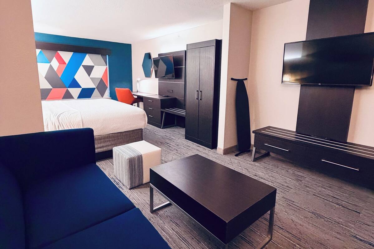 A hotel room with a bed, a sofa, a TV, a desk, and a wardrobe.