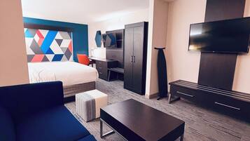 Una habitación de hotel con cama, sofá, televisión, escritorio y armario.