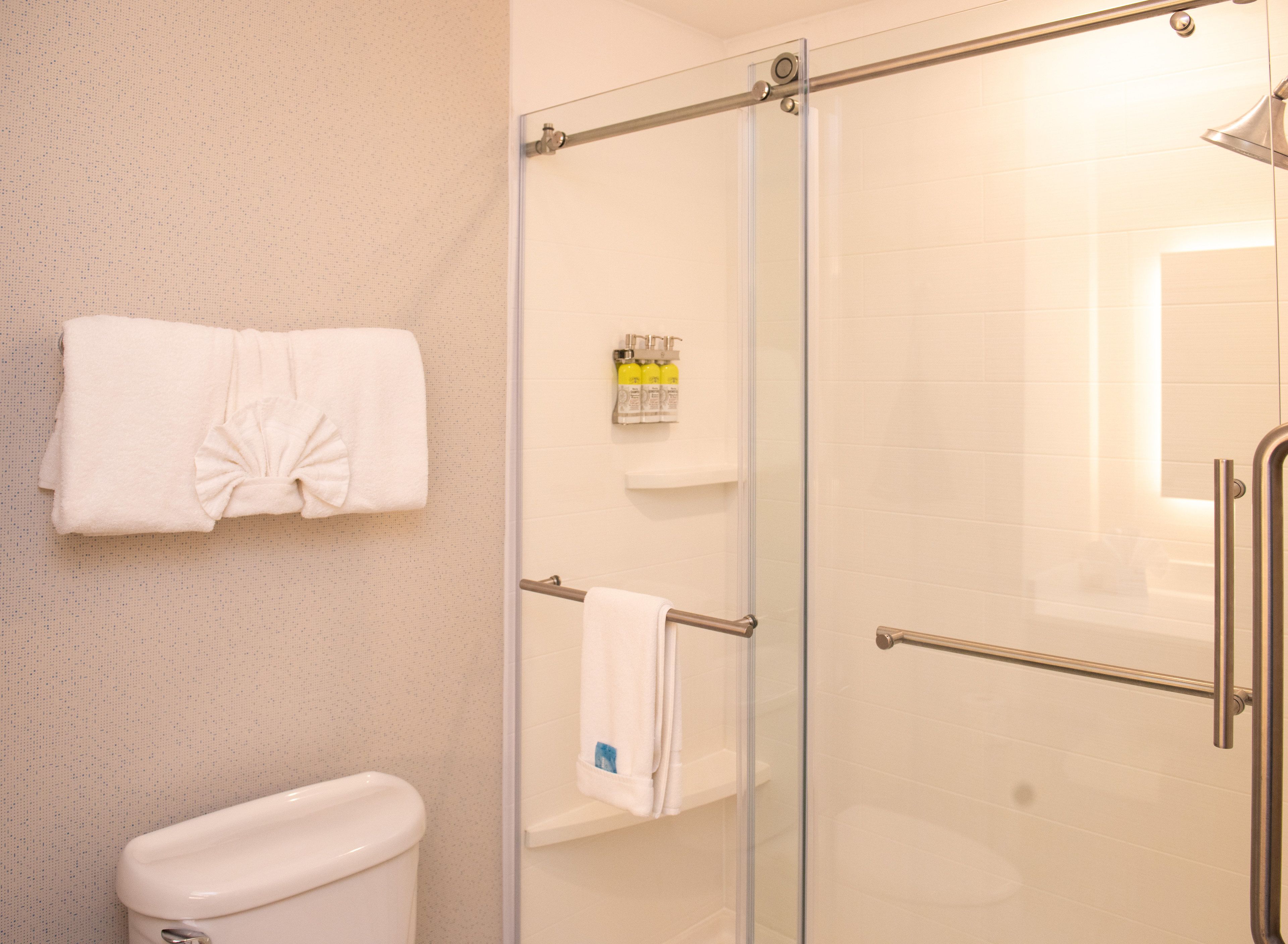 A bathroom with a glass shower enclosure, a toilet, and two towels hanging on the wall.