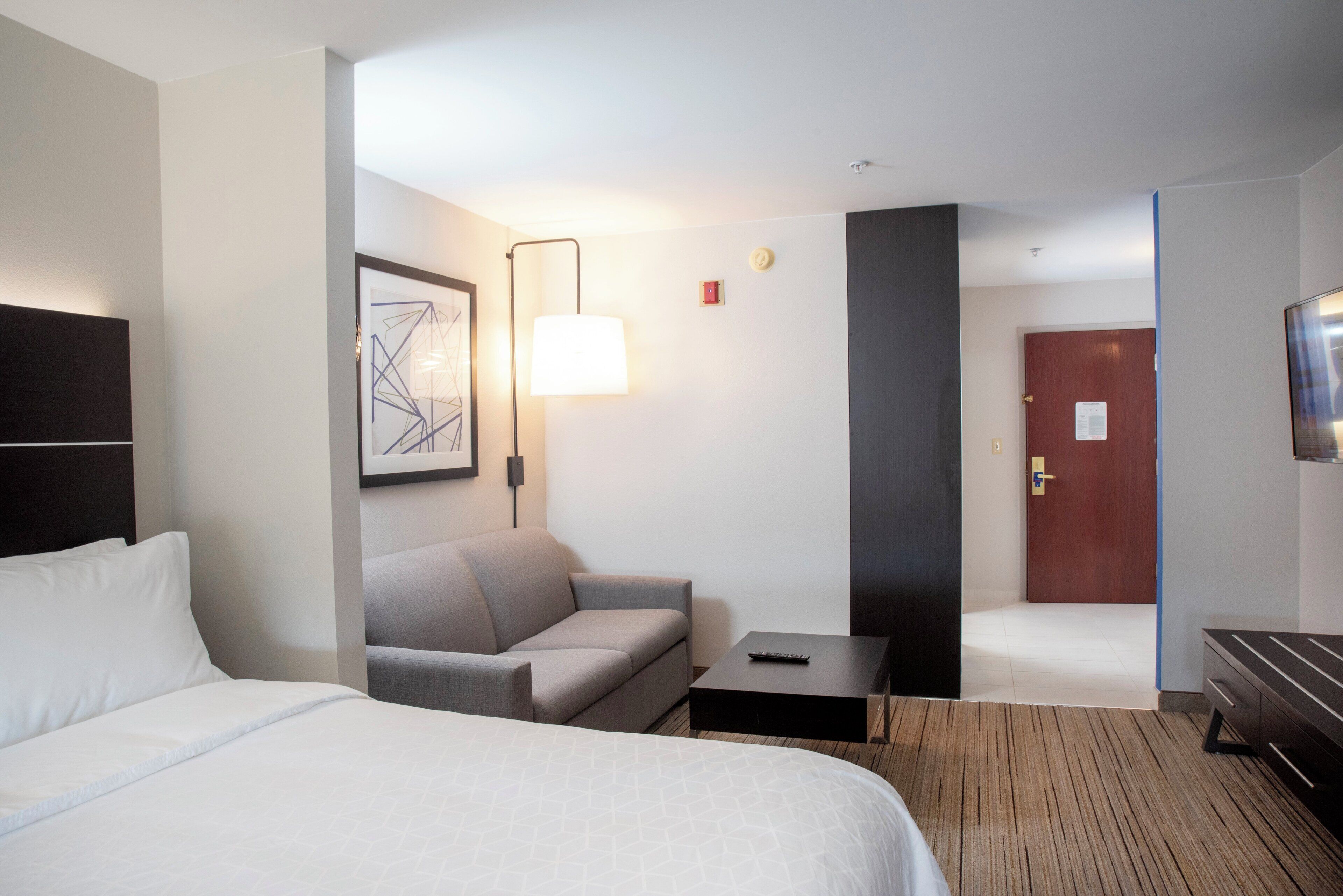 A hotel room with a bed, a sofa, a small table, a lamp, and a door.