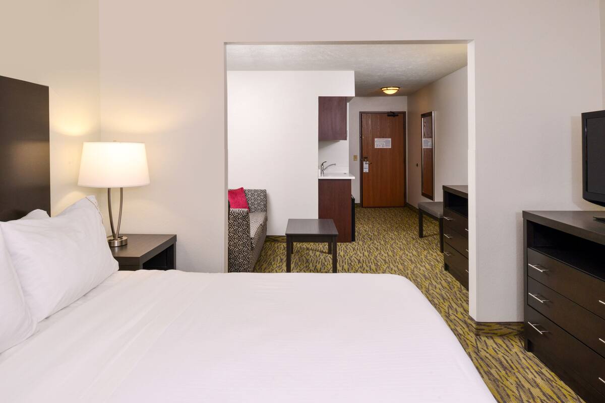 A hotel room with a bed, a nightstand with a lamp, a desk, a chair, a wardrobe, and a television.