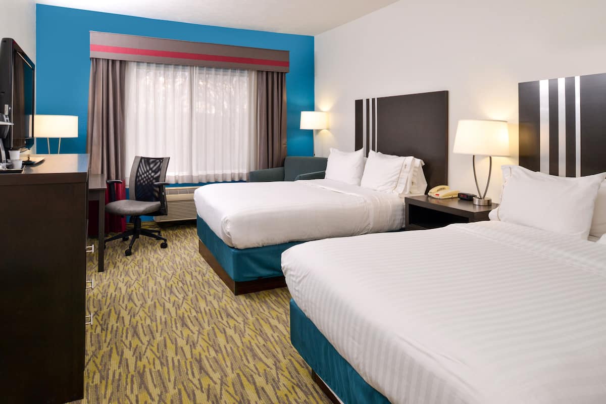 A hotel room with two beds, a desk, a chair, a desk lamp, a telephone, and a window with curtains.