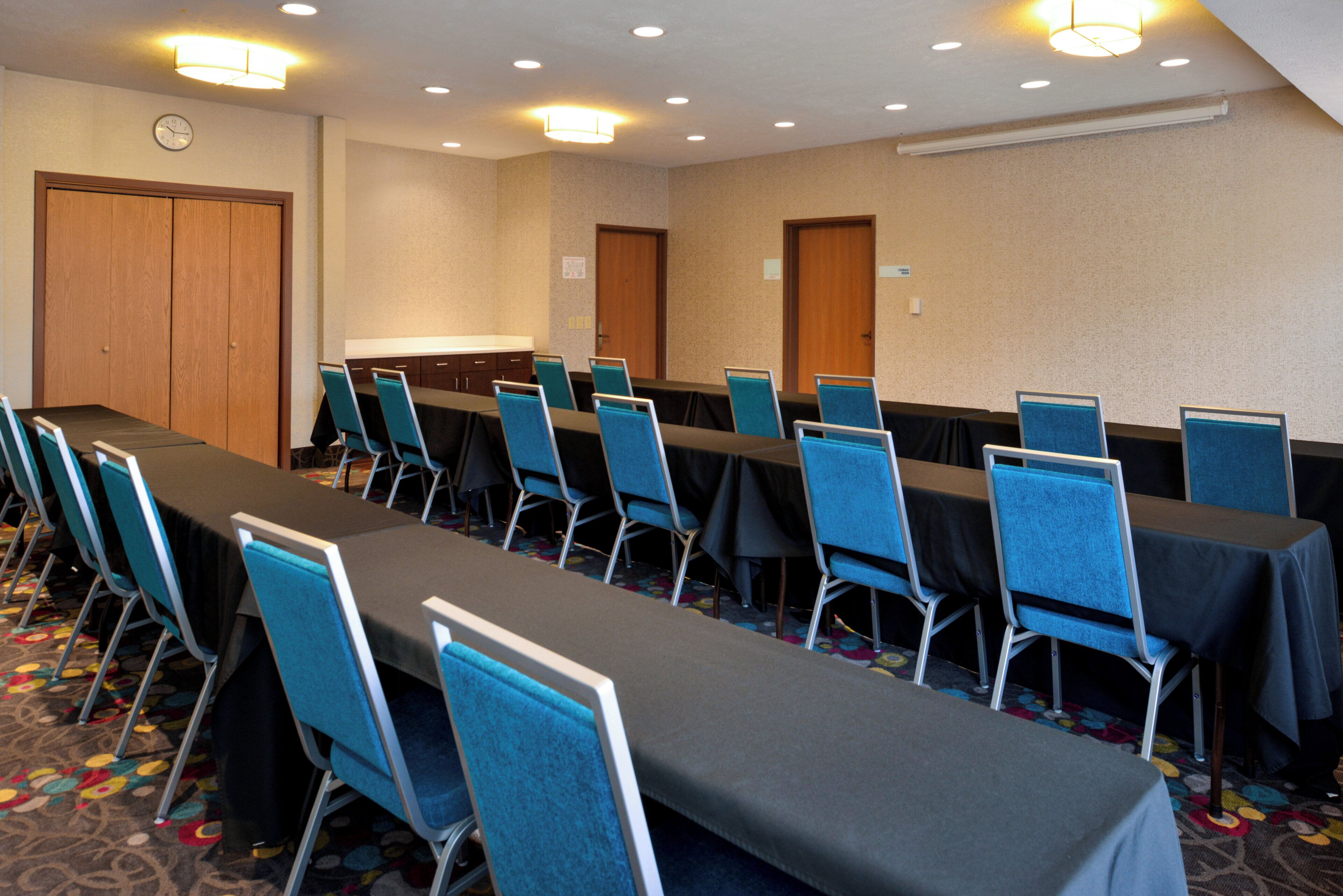 A conference room with a long table, blue chairs, and carpeted flooring.