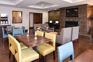A hotel lobby with a dining area, sofas, a fireplace, and a TV mounted on the wall.